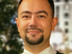 A head shot of Vlad wearing a white bow tie, formal shirt and grey waistcoat, he is looking straight ahead, smiling slightly